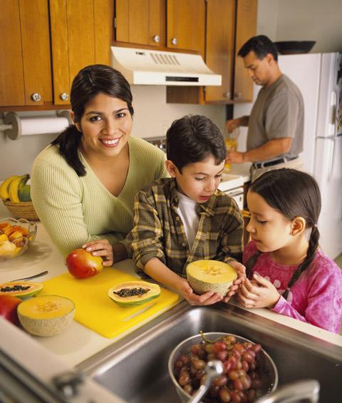 Hispanic family making fruit salad. Involve the kids in making lunch says Bridget Swinney at www.eatrightmama.com