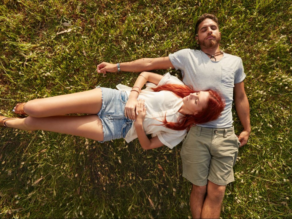 Young man and woman lying on the lawn sleeping. Overhead view of young couple resting together on the grass.